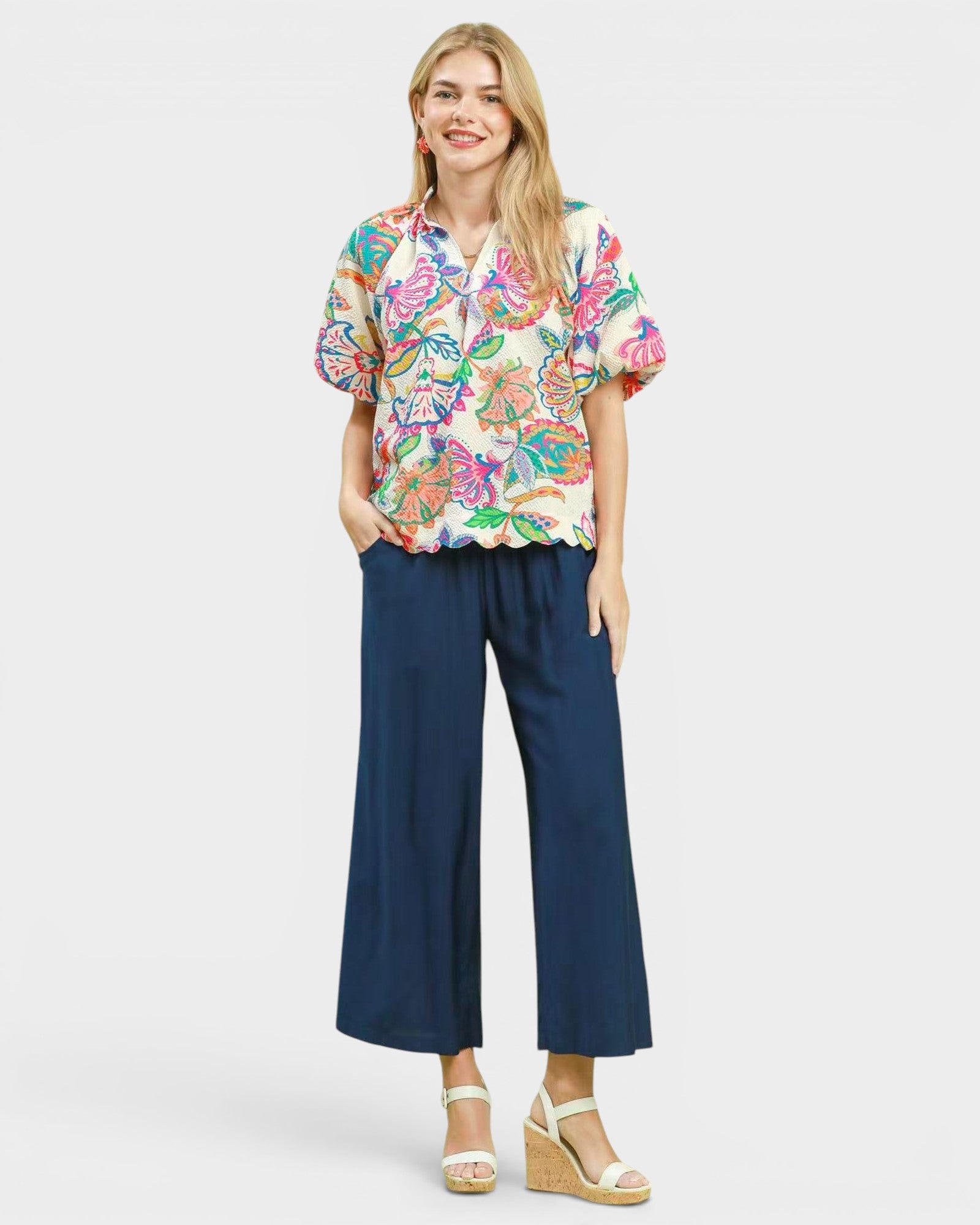 Woman wearing a colorful floral blouse and navy pants on a white background