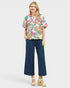 Woman wearing a colorful floral blouse and navy pants on a white background