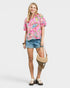 Woman wearing a colorful shirt and denim shorts, holding a bag on a white background