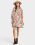 A woman modeling a long-sleeve floral shirt dress with a high collar, paired with a wide-brimmed straw hat and brown ankle boots, against a light gray studio background.