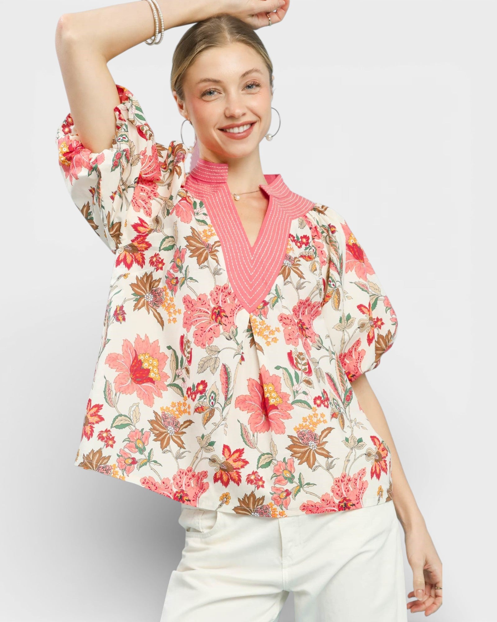 Woman wearing a floral blouse over a pink sweater on a light gray background