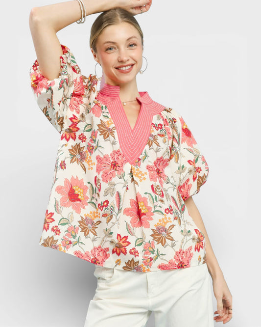 Woman wearing a floral blouse over a pink sweater on a light gray background