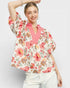Woman wearing a floral blouse over a pink sweater on a light gray background