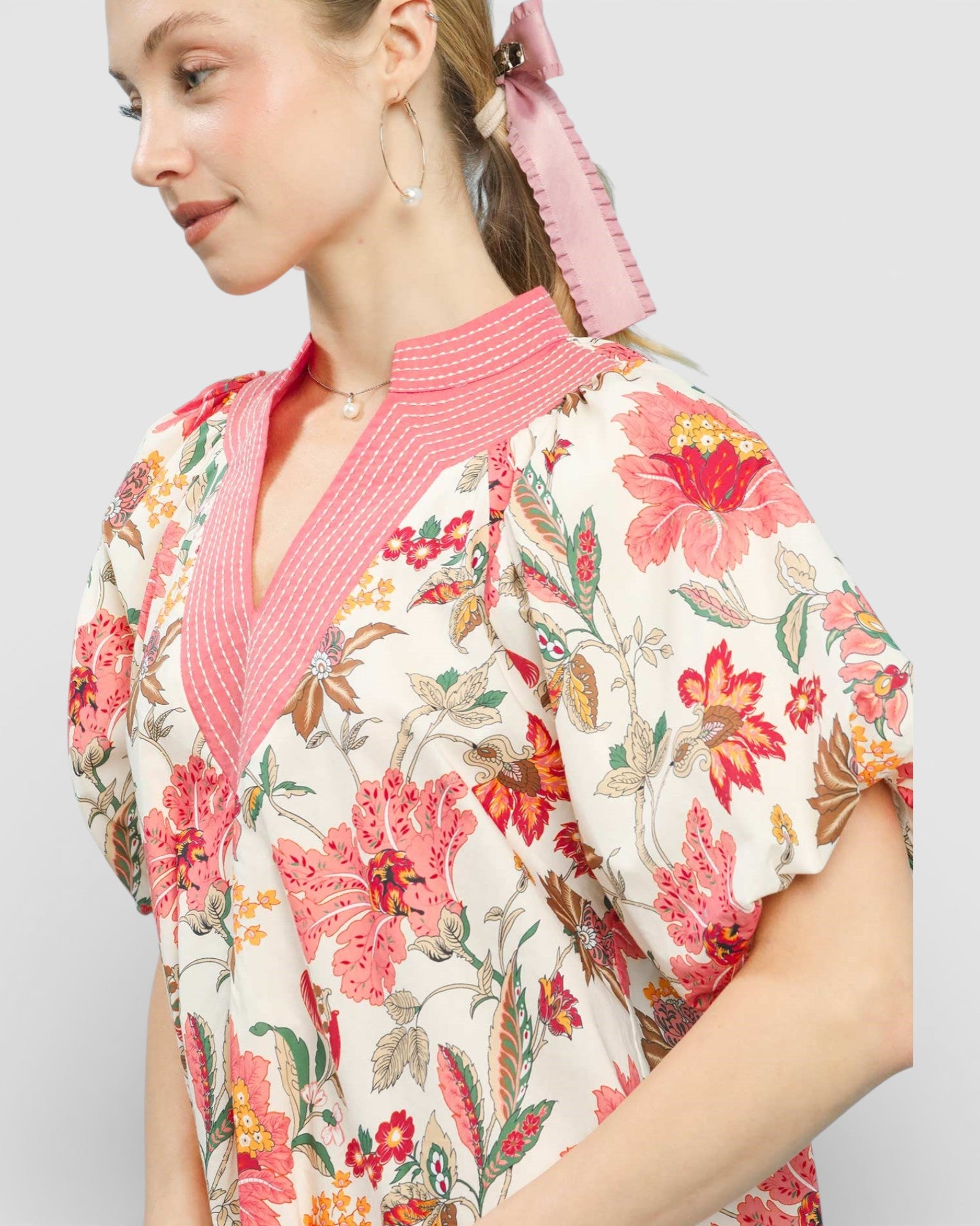 Woman wearing a floral blouse with a pink collar against a plain background