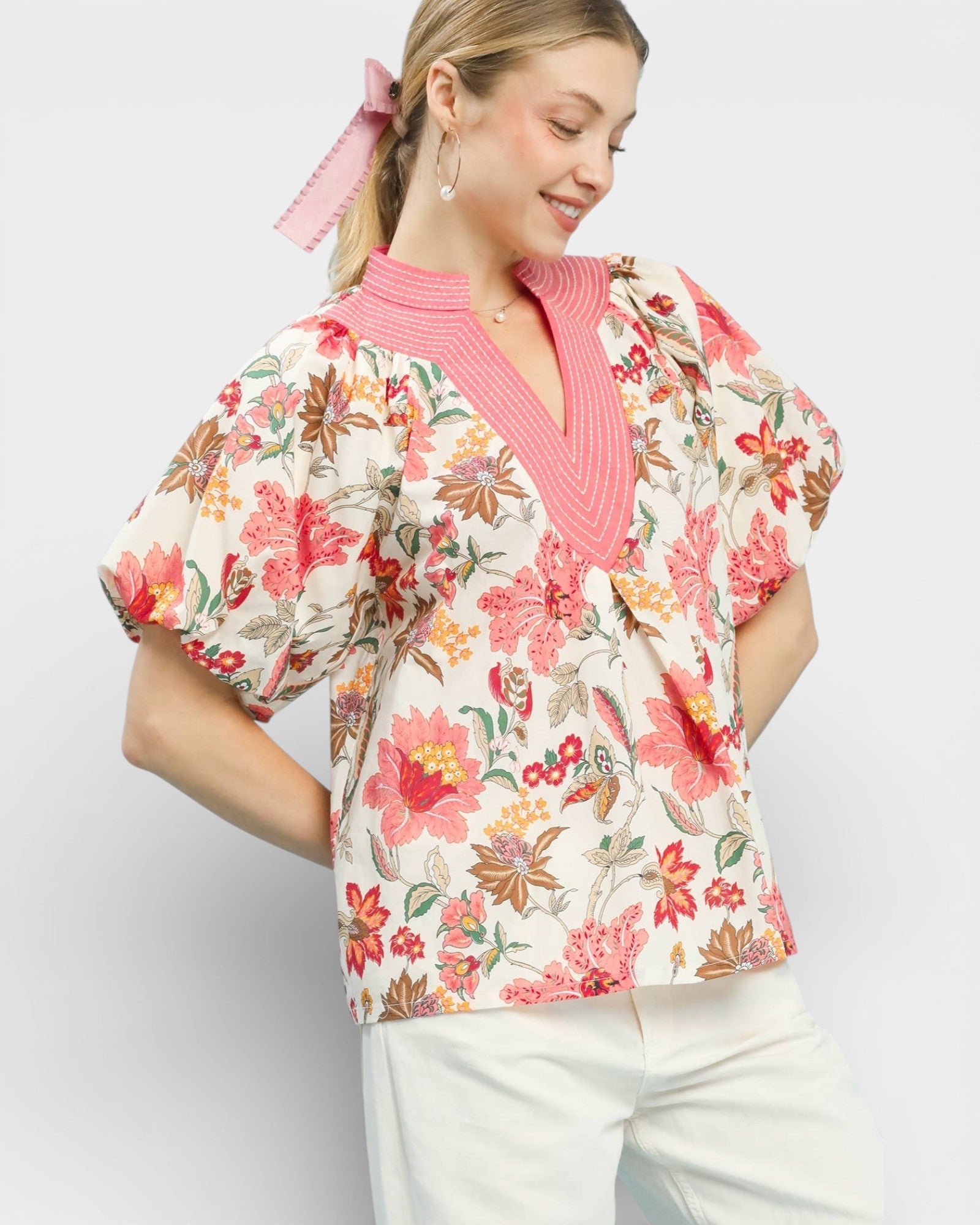 Woman wearing a floral blouse with a pink collar against a white background