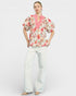 Woman wearing a floral blouse and white pants on a white background