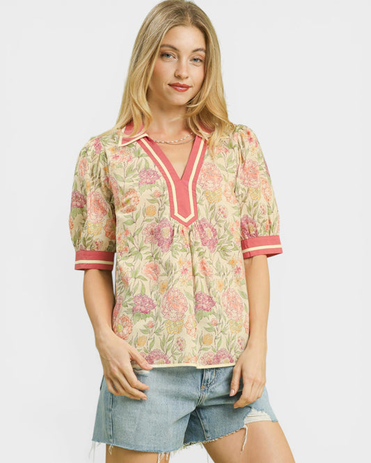 Woman wearing a floral blouse with pink accents and denim shorts on a white background