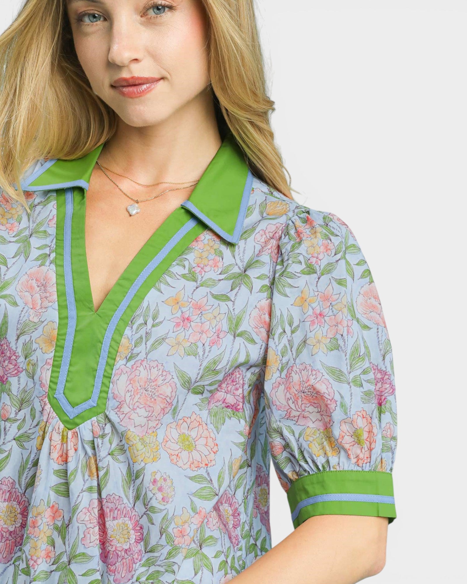 Woman wearing a floral blouse with green accents on a plain background