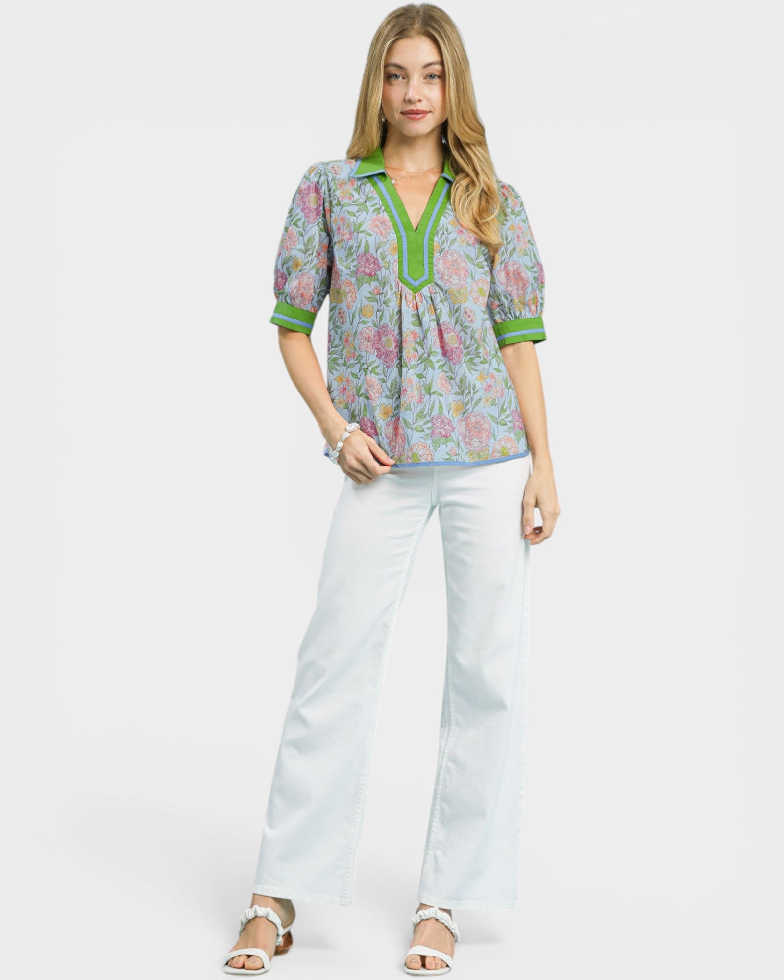 Woman wearing a patterned blouse and white pants on a white background