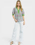 Woman wearing a patterned blouse and white pants on a white background