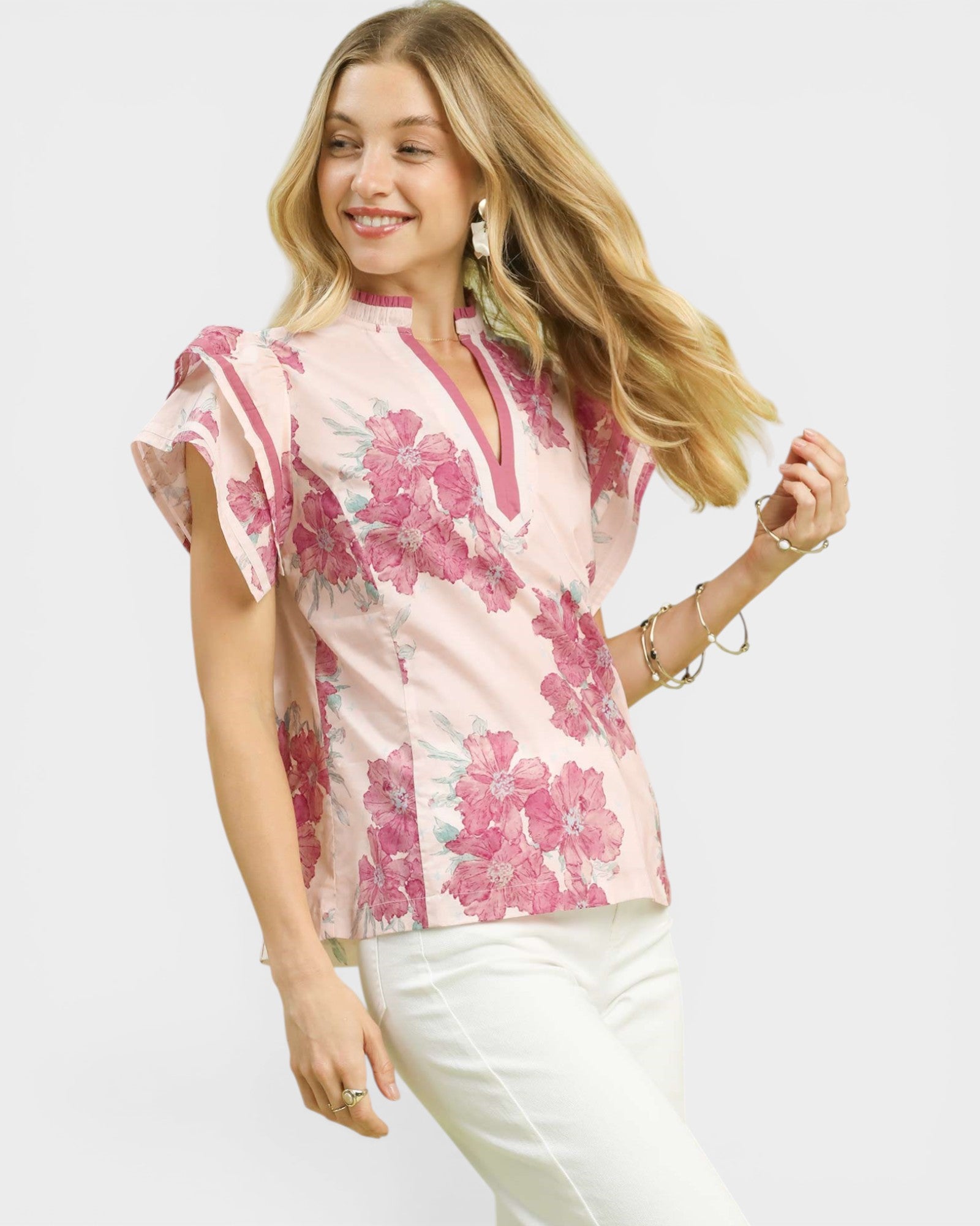 Woman wearing a pink floral blouse with white pants on a light gray background