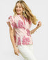 Woman wearing a pink floral blouse with white pants on a light gray background