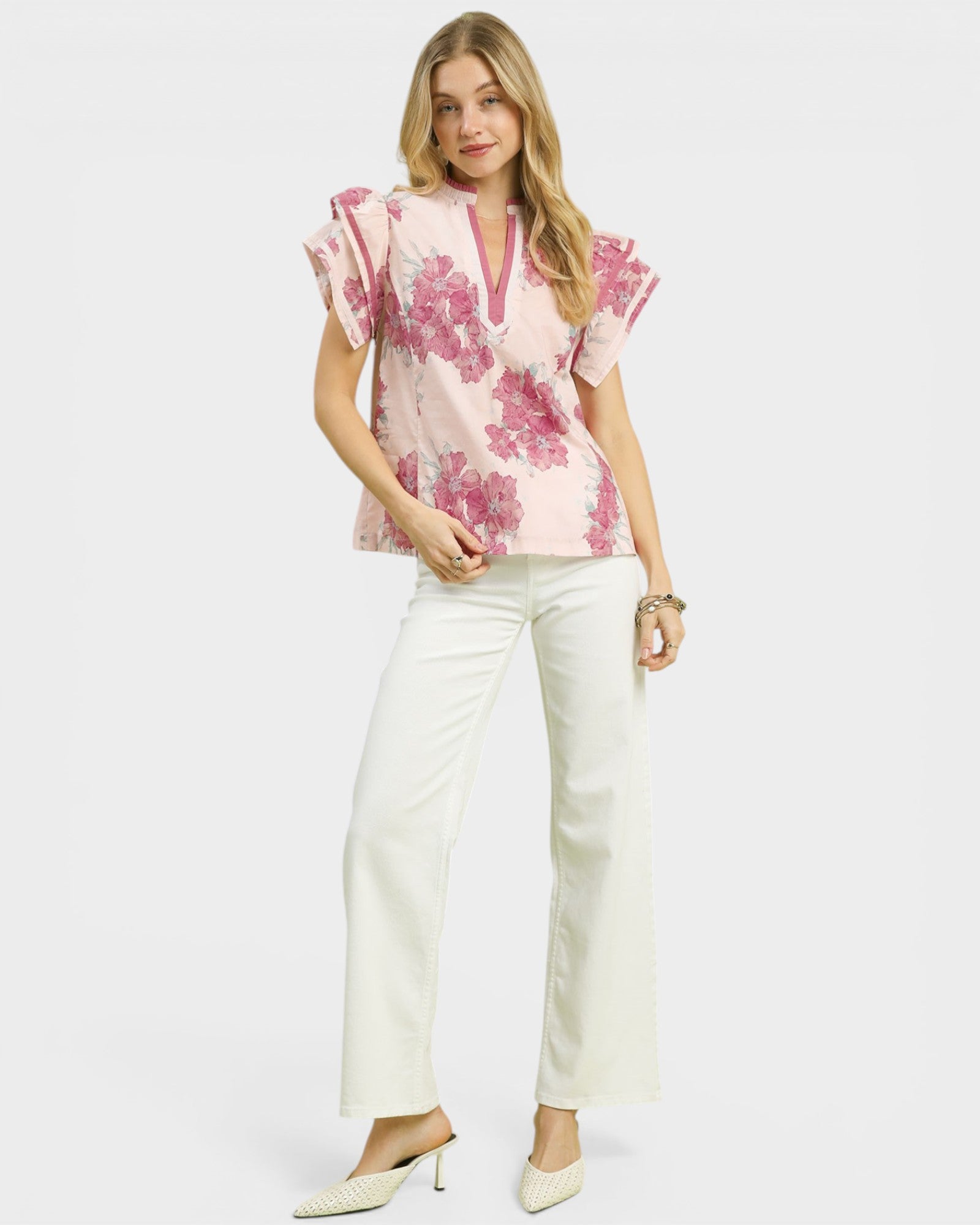 Woman wearing a pink floral blouse and white pants on a white background