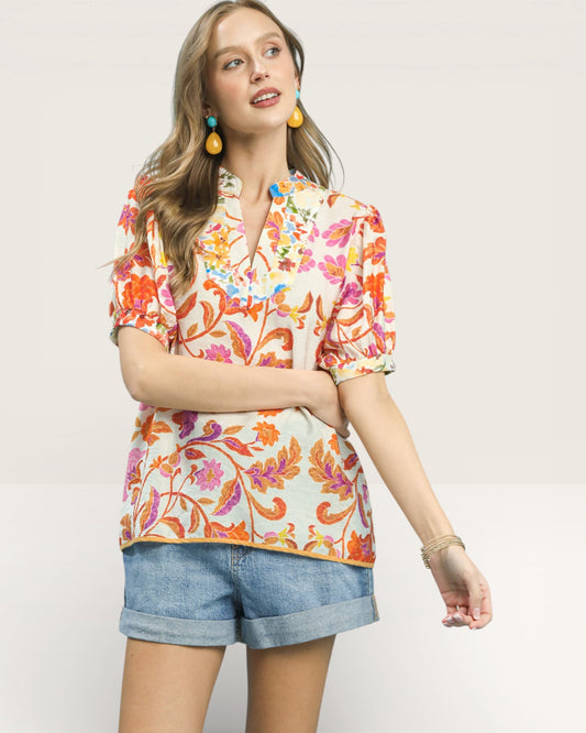Woman wearing a colorful floral blouse and denim shorts on a plain background