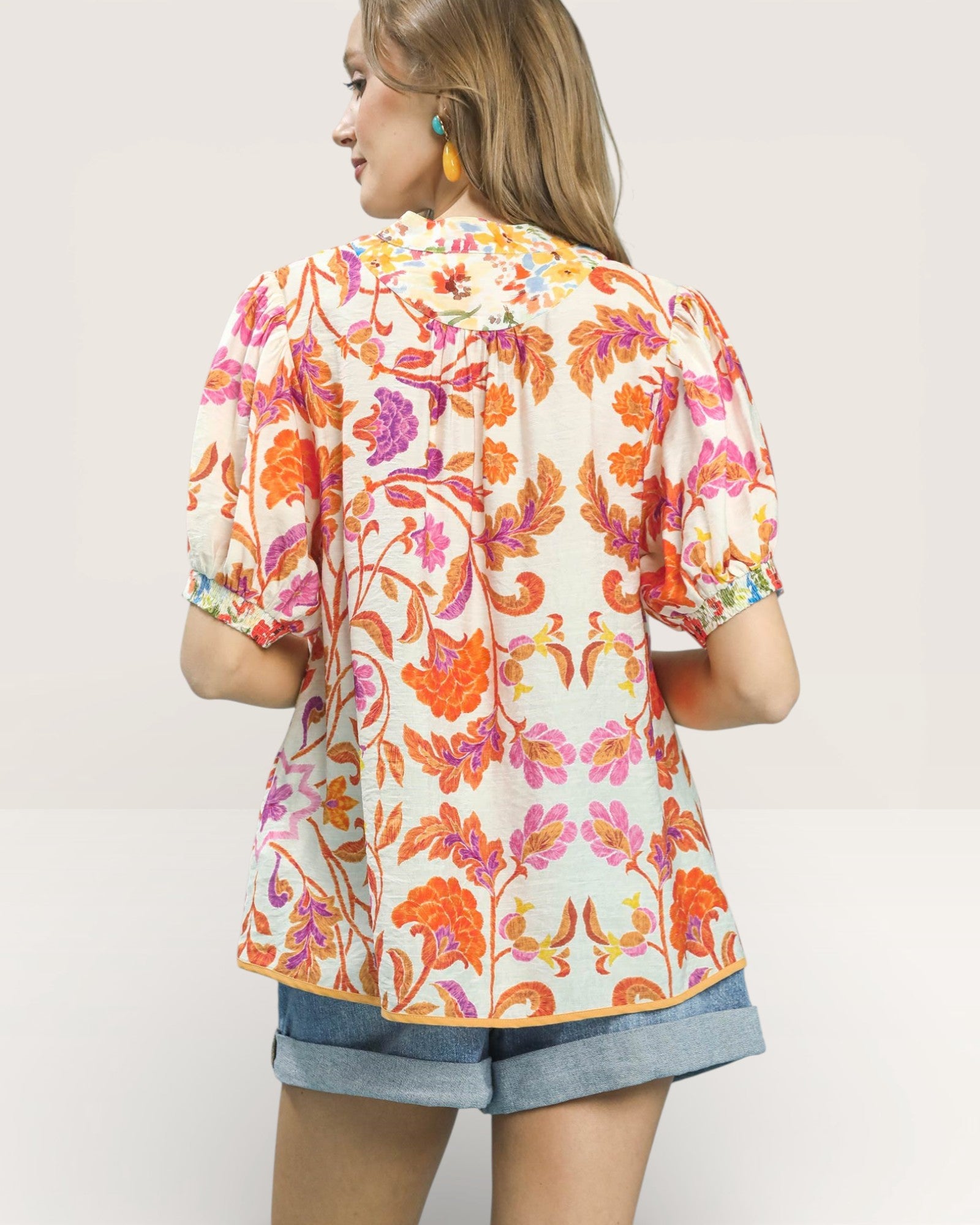 Woman wearing a colorful floral blouse with denim shorts on a plain background