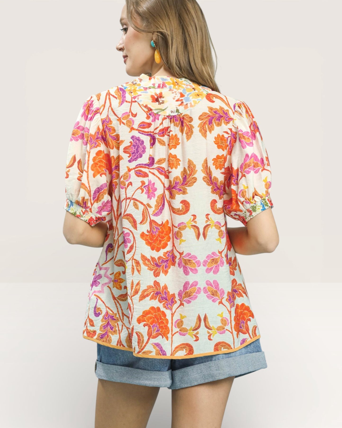 Woman wearing a colorful floral blouse with denim shorts on a plain background