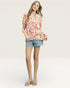 Woman wearing a colorful floral blouse and denim shorts on a white background