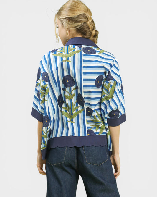 Person wearing a blue and white striped shirt with floral patterns on a plain background