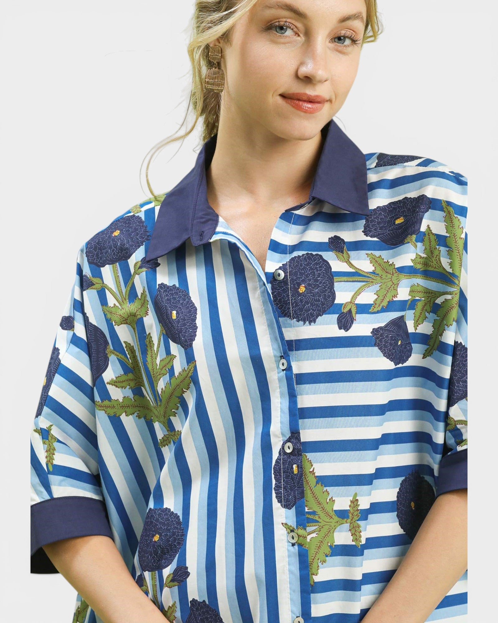 Woman wearing a blue and white striped shirt with floral patterns on a plain background