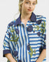 Woman wearing a blue and white striped shirt with floral patterns on a plain background