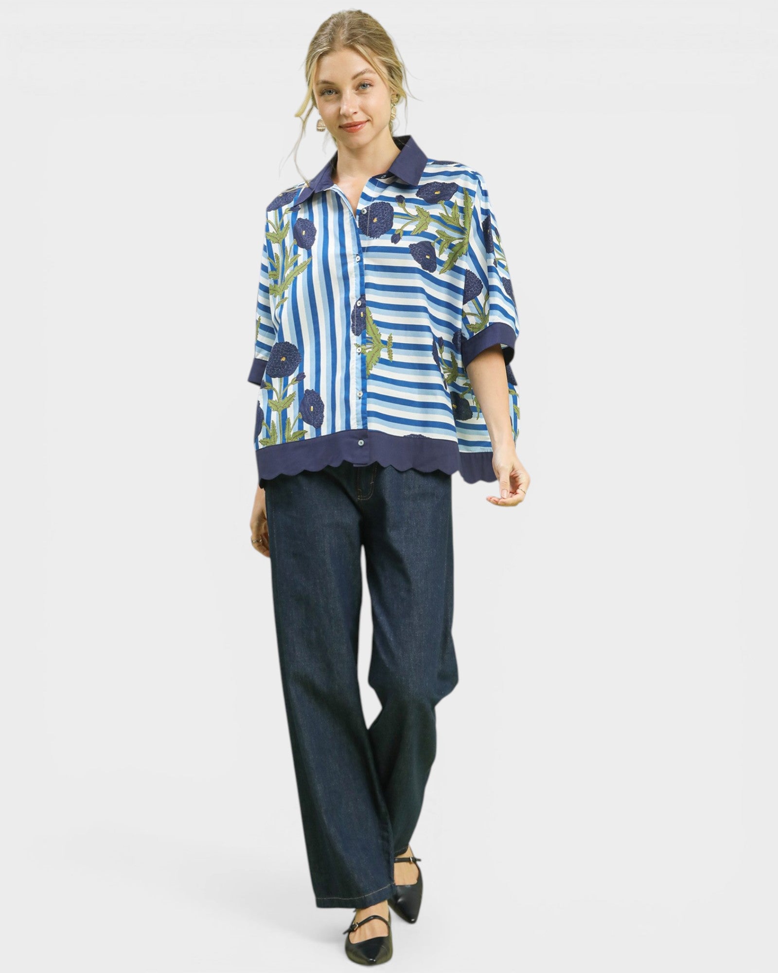 Woman wearing a blue and white striped shirt with floral patterns and dark jeans on a light gray background