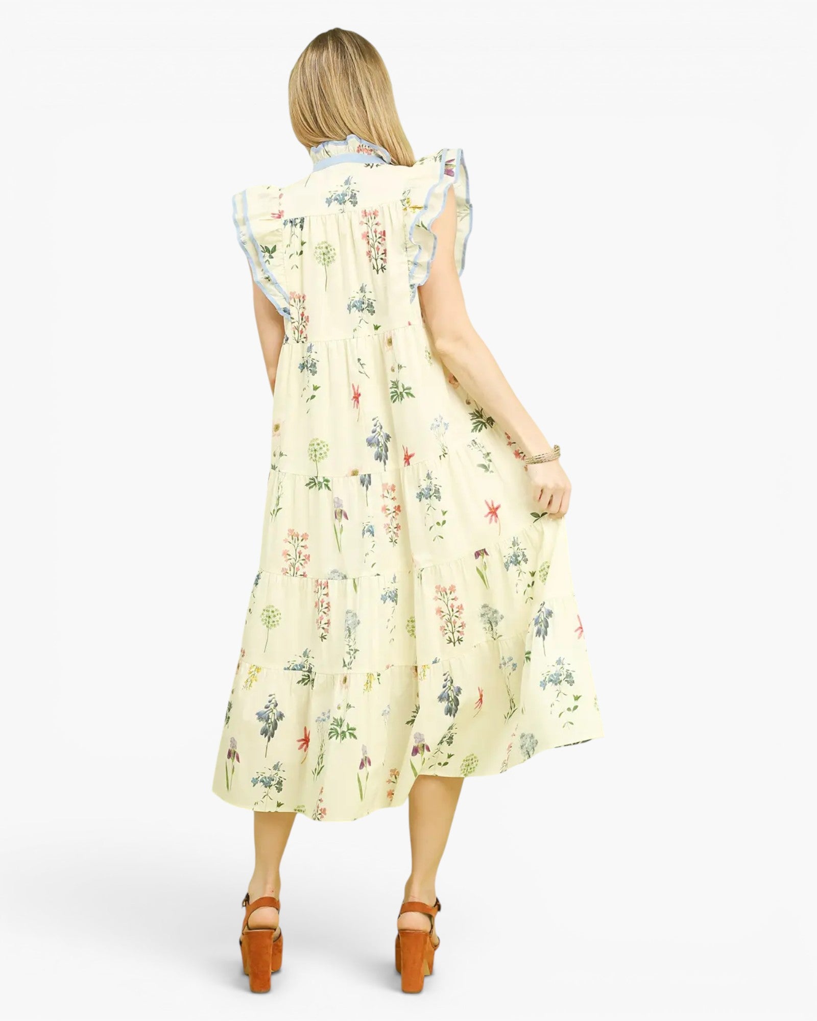 A woman shown from the back wearing a sleeveless midi dress with a light cream base and a delicate multicolor floral print. The dress features ruffled cap sleeves and a gathered waist.