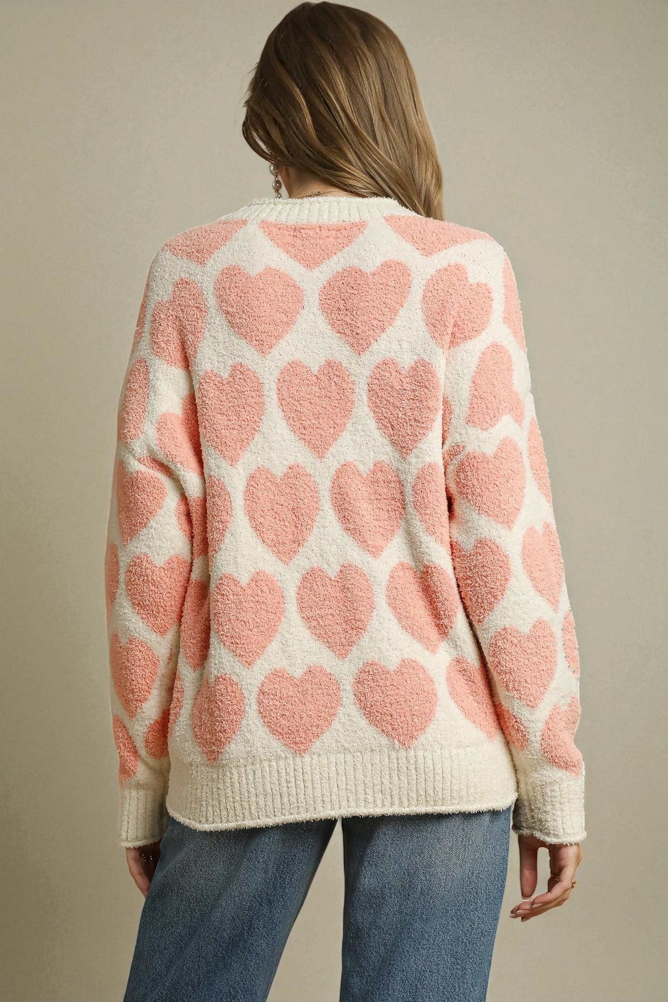 Person wearing a sweater with pink heart patterns on a beige background