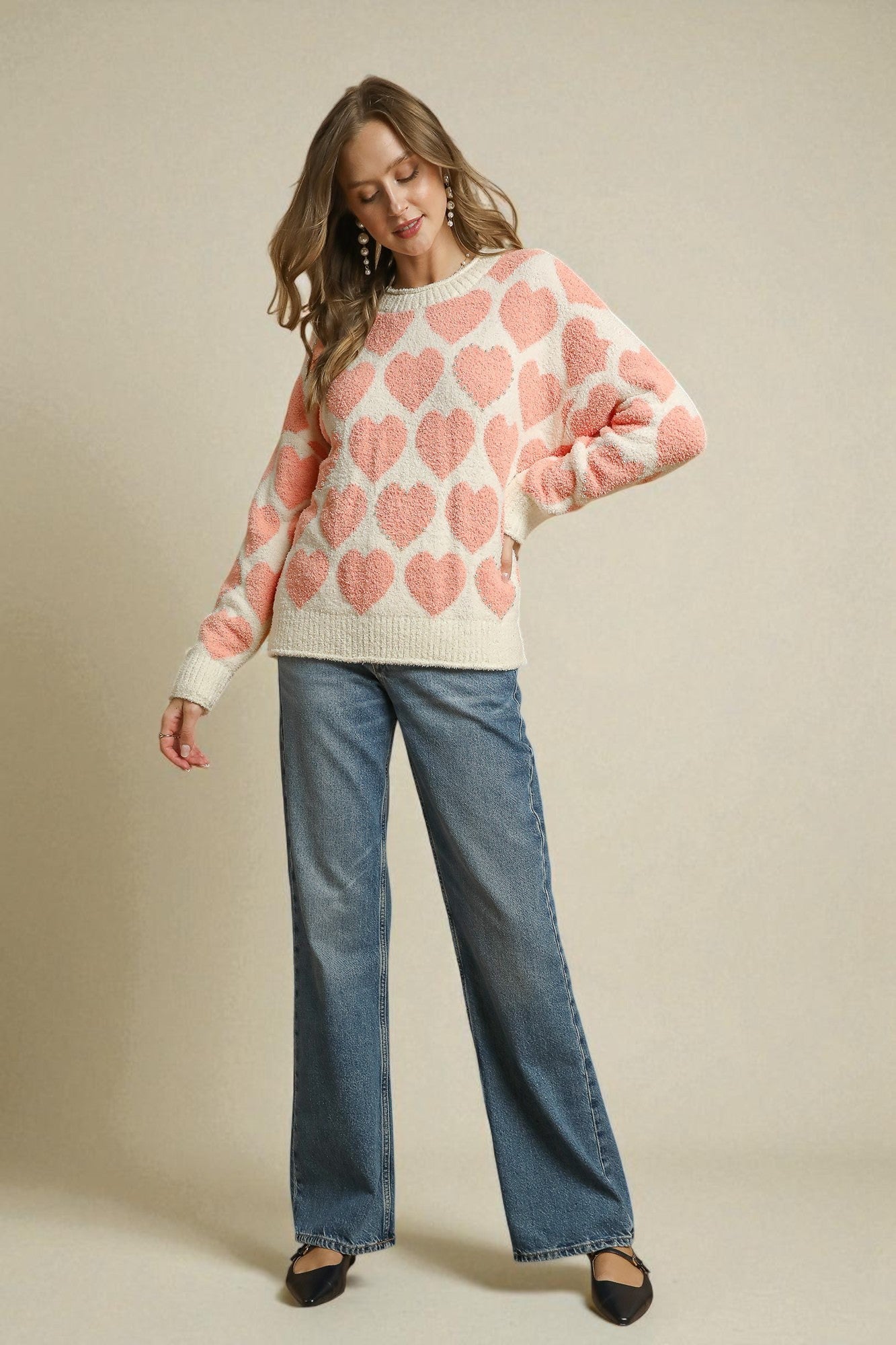 Woman wearing a pink heart-patterned sweater and blue jeans on a beige background