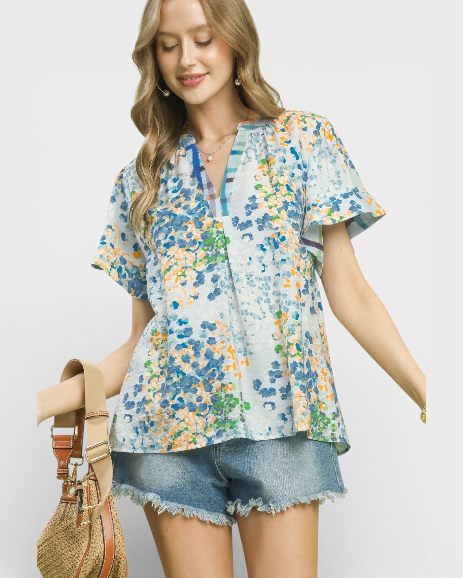 Woman wearing a floral blouse and denim shorts with a straw bag on a white background