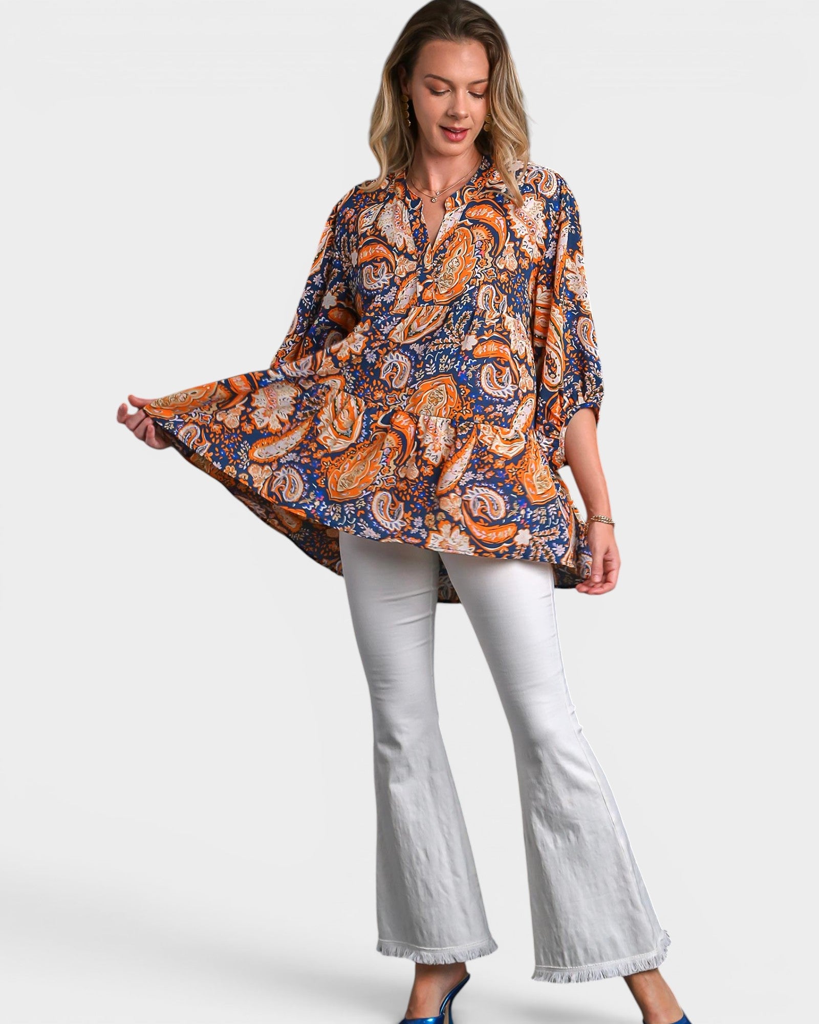 Woman wearing a patterned blouse and white pants on a white background