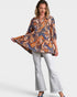 Woman wearing a patterned blouse and white pants on a white background