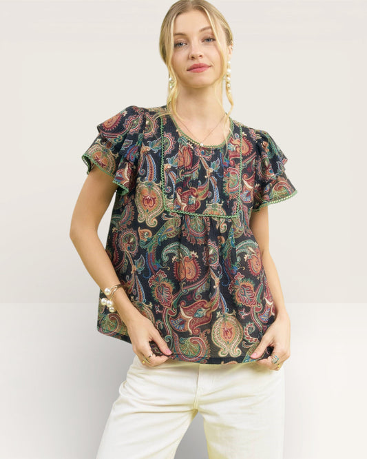 Woman wearing a patterned top with ruffled sleeves on a plain background