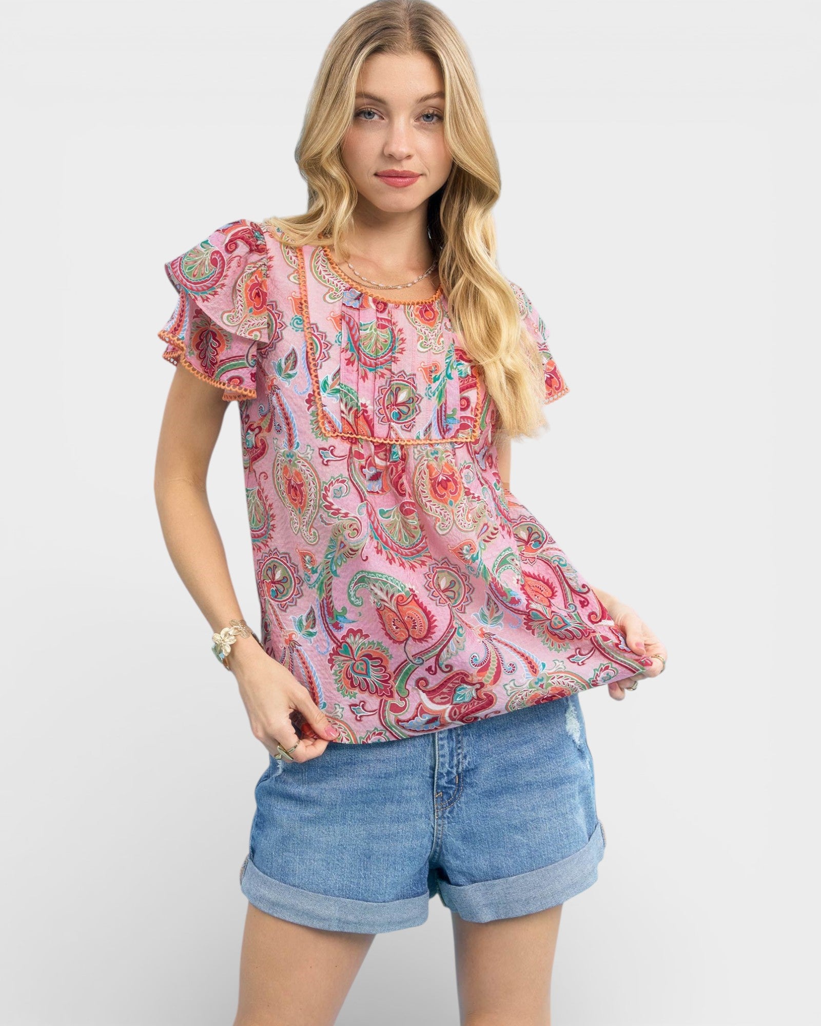 Woman wearing a colorful paisley top and denim shorts on a white background