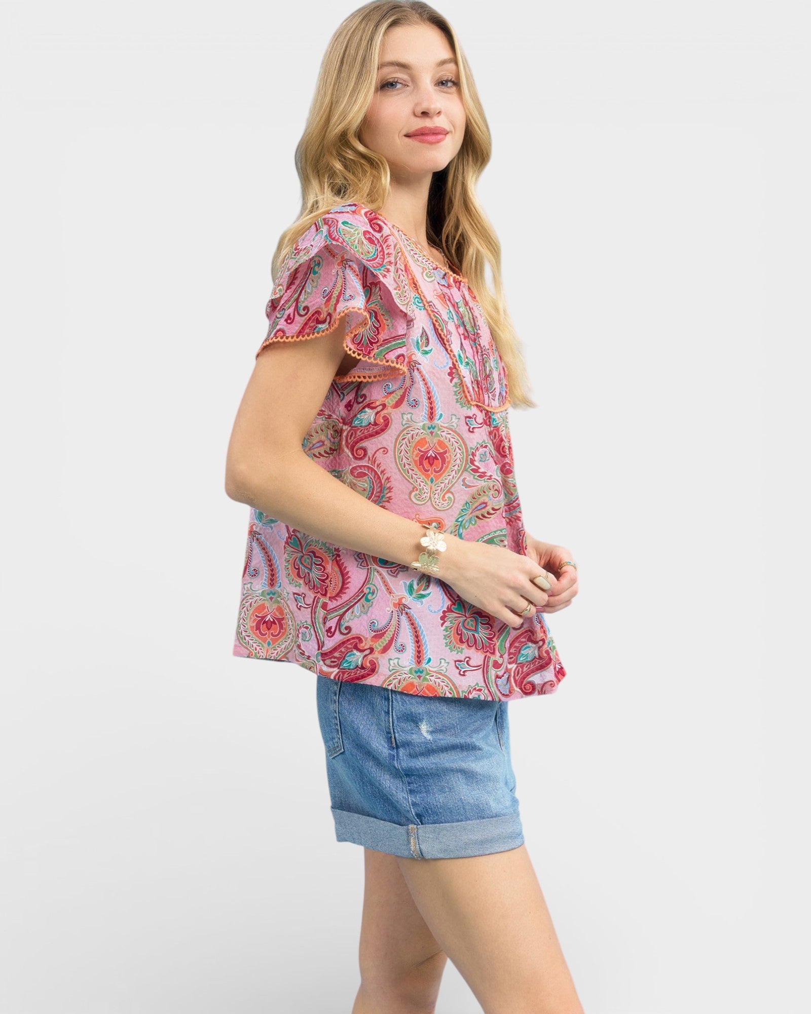 Woman wearing a colorful patterned blouse and denim shorts on a white background