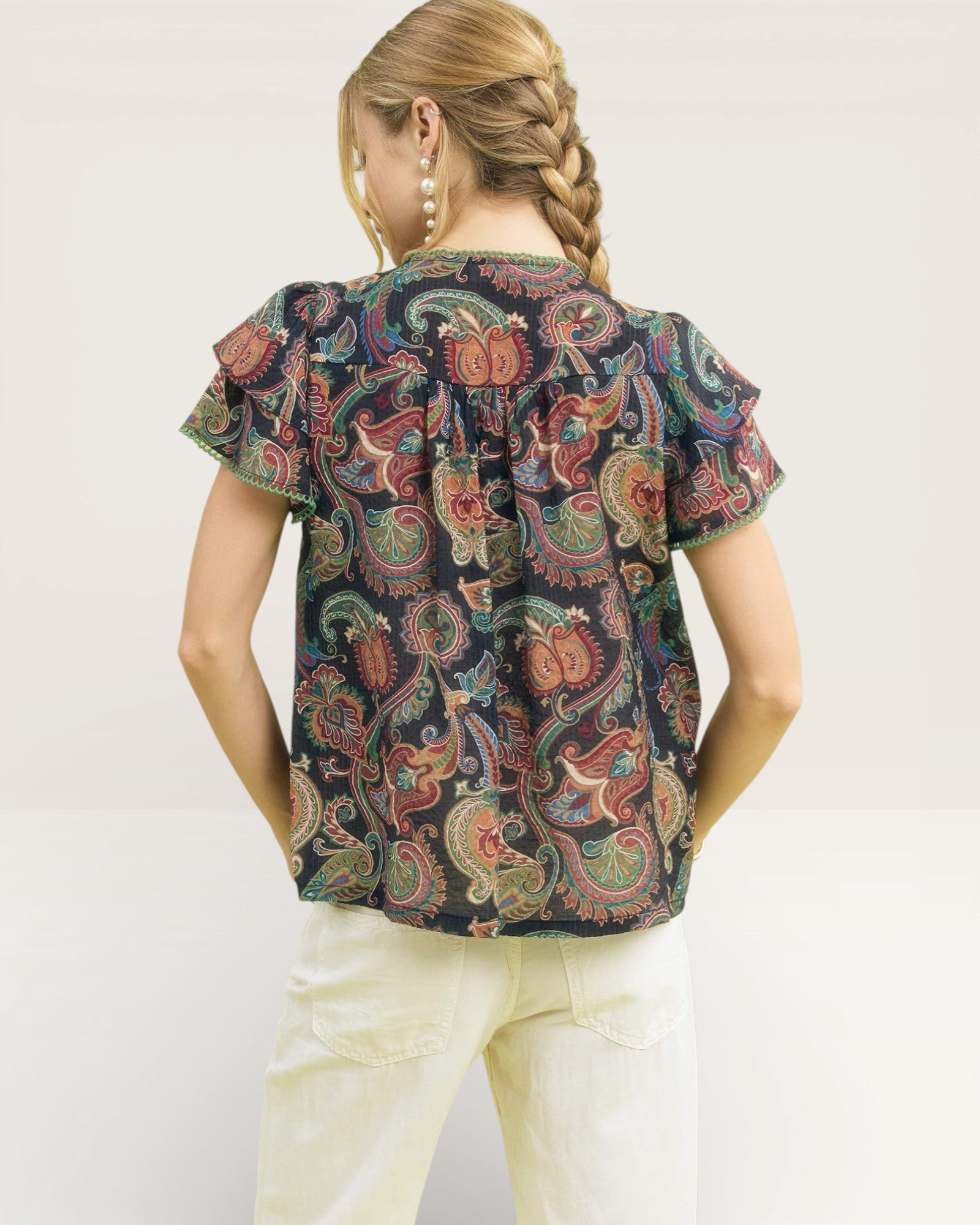 Girl wearing a patterned top and white pants on a plain background