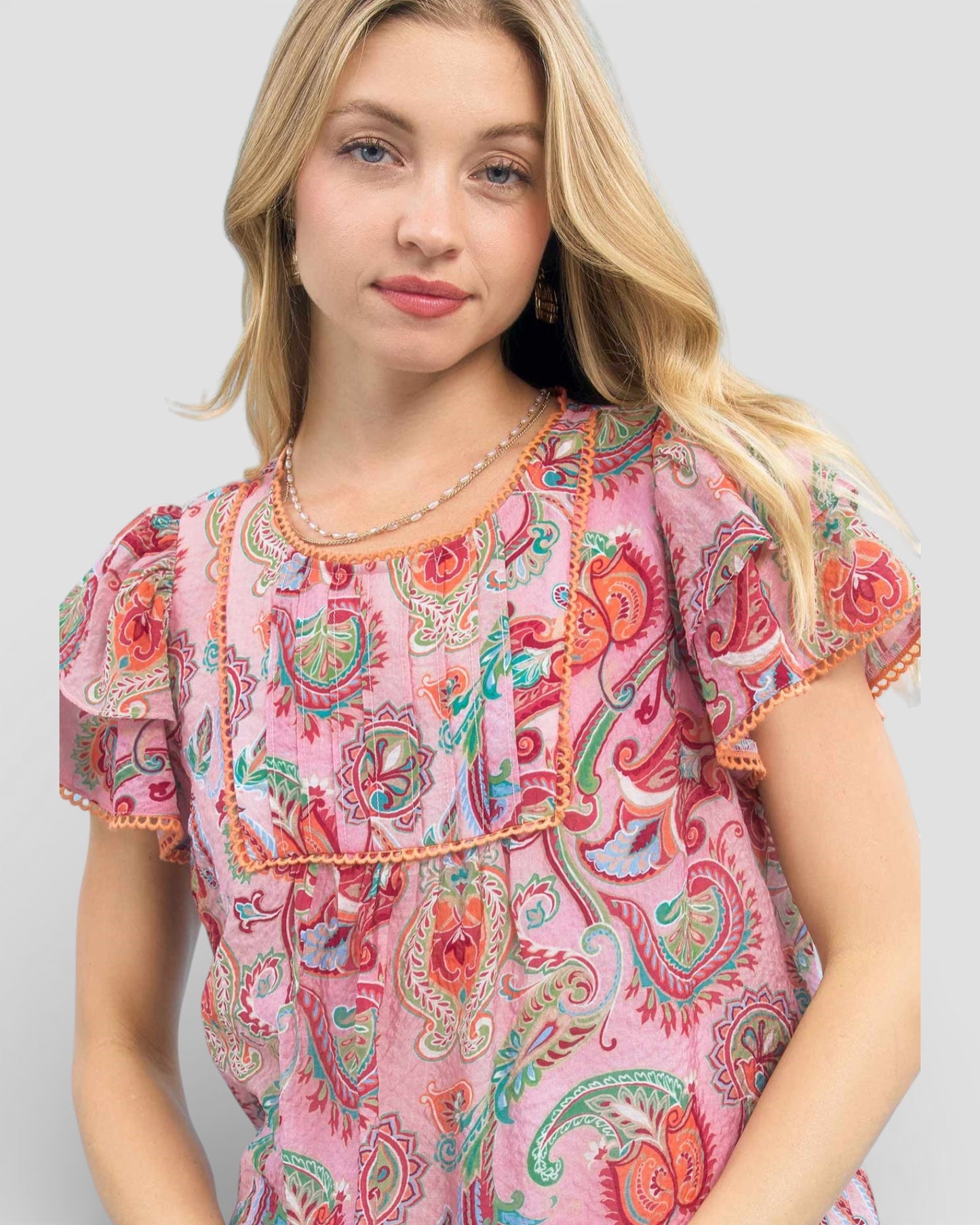 Woman wearing a pink paisley dress against a plain background