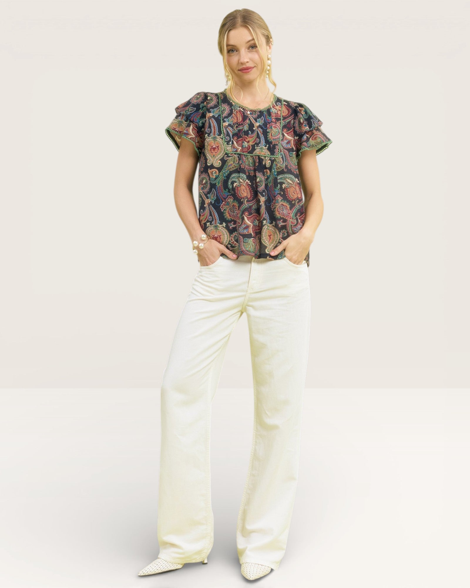 Woman wearing a floral top and white pants on a white background