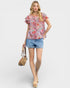Woman wearing a floral blouse and denim shorts with a handbag on a white background