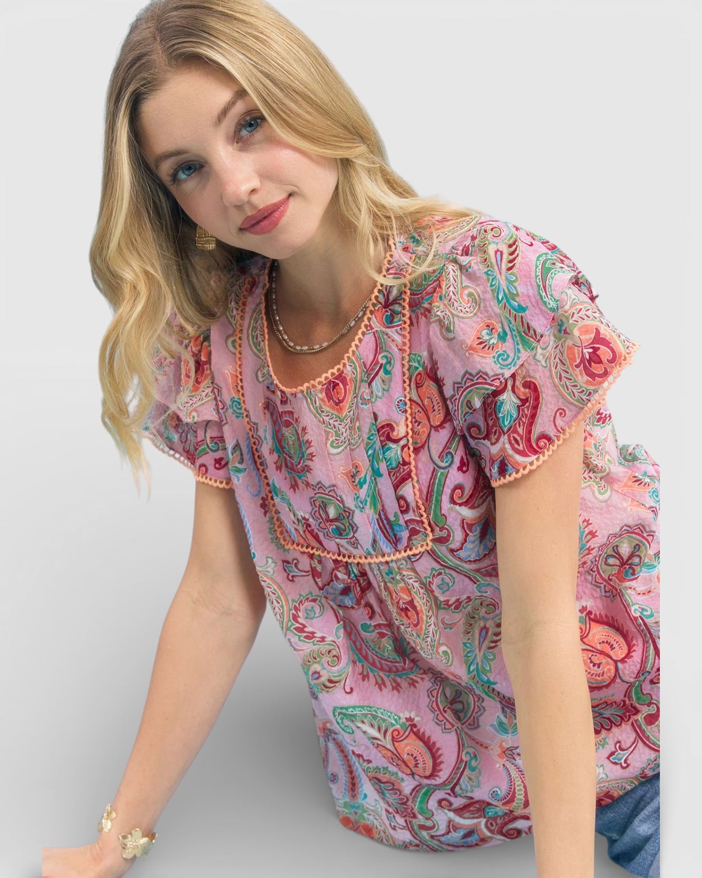 Woman wearing a pink paisley patterned top on a white background