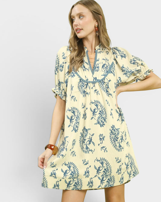 Woman wearing a yellow dress with blue floral pattern on a plain background