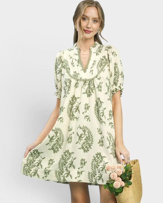 Woman wearing a floral dress holding flowers against a plain background