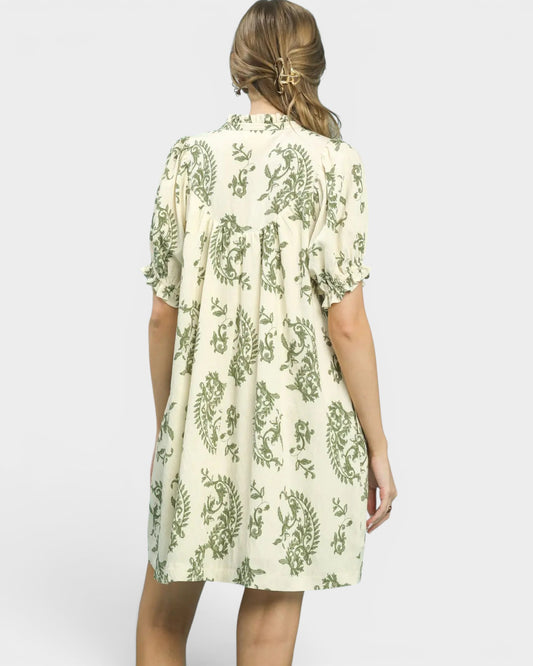 Woman wearing a white dress with green floral pattern on a plain background