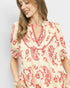 Woman wearing a cream and red patterned blouse against a plain background