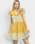 A young woman modeling a yellow and white patterned dress with ruffled sleeves and tiered skirt, photographed against a light gray studio background.