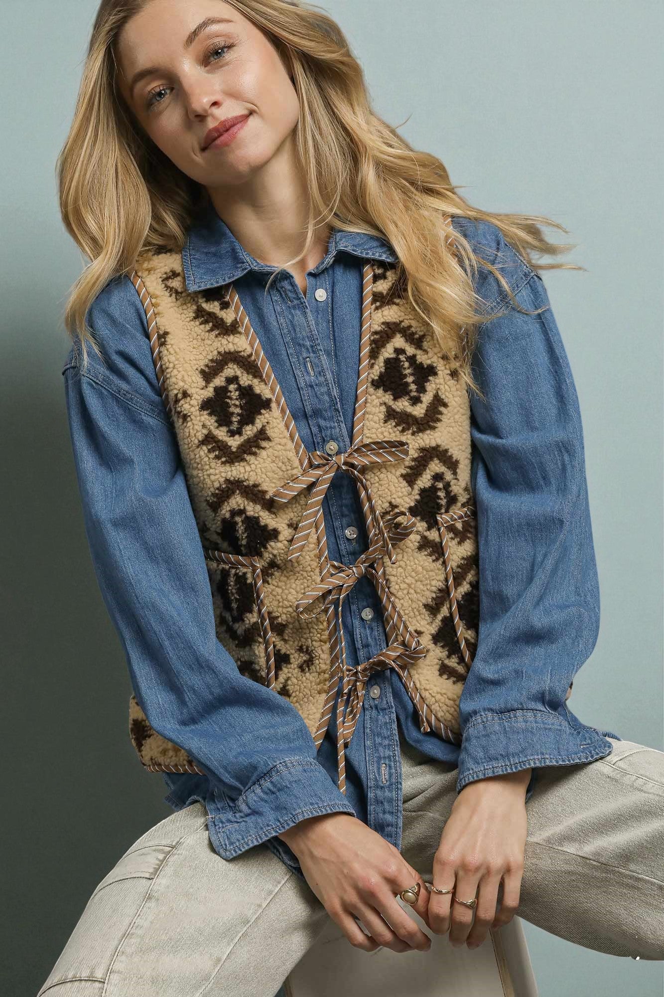 Woman wearing a denim shirt and patterned vest against a neutral background