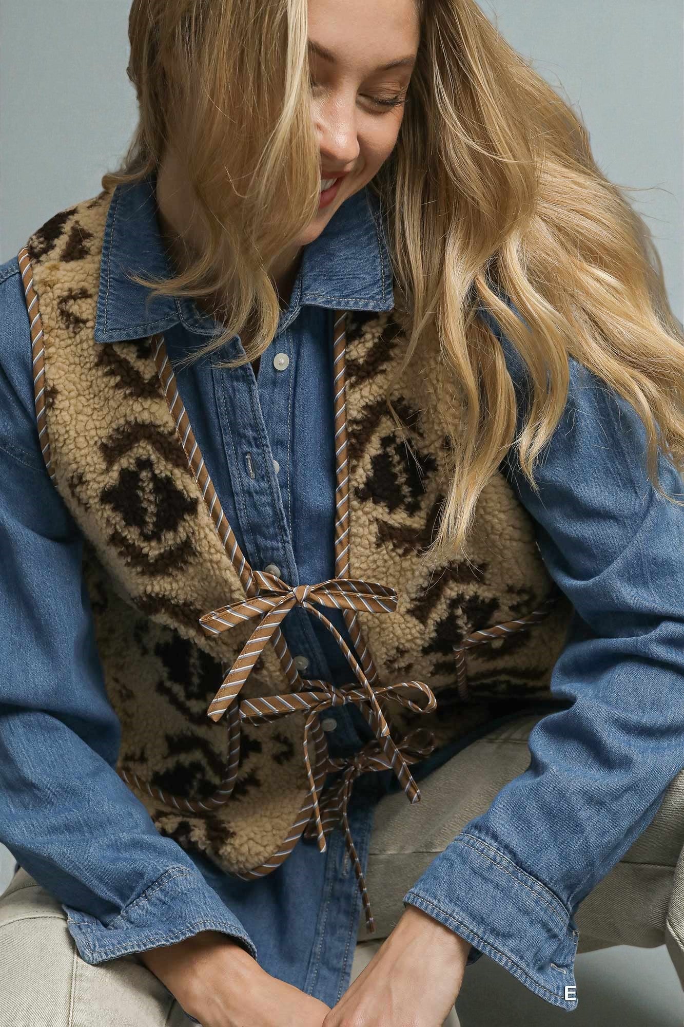 Woman wearing a leopard print vest over a denim shirt against a neutral background