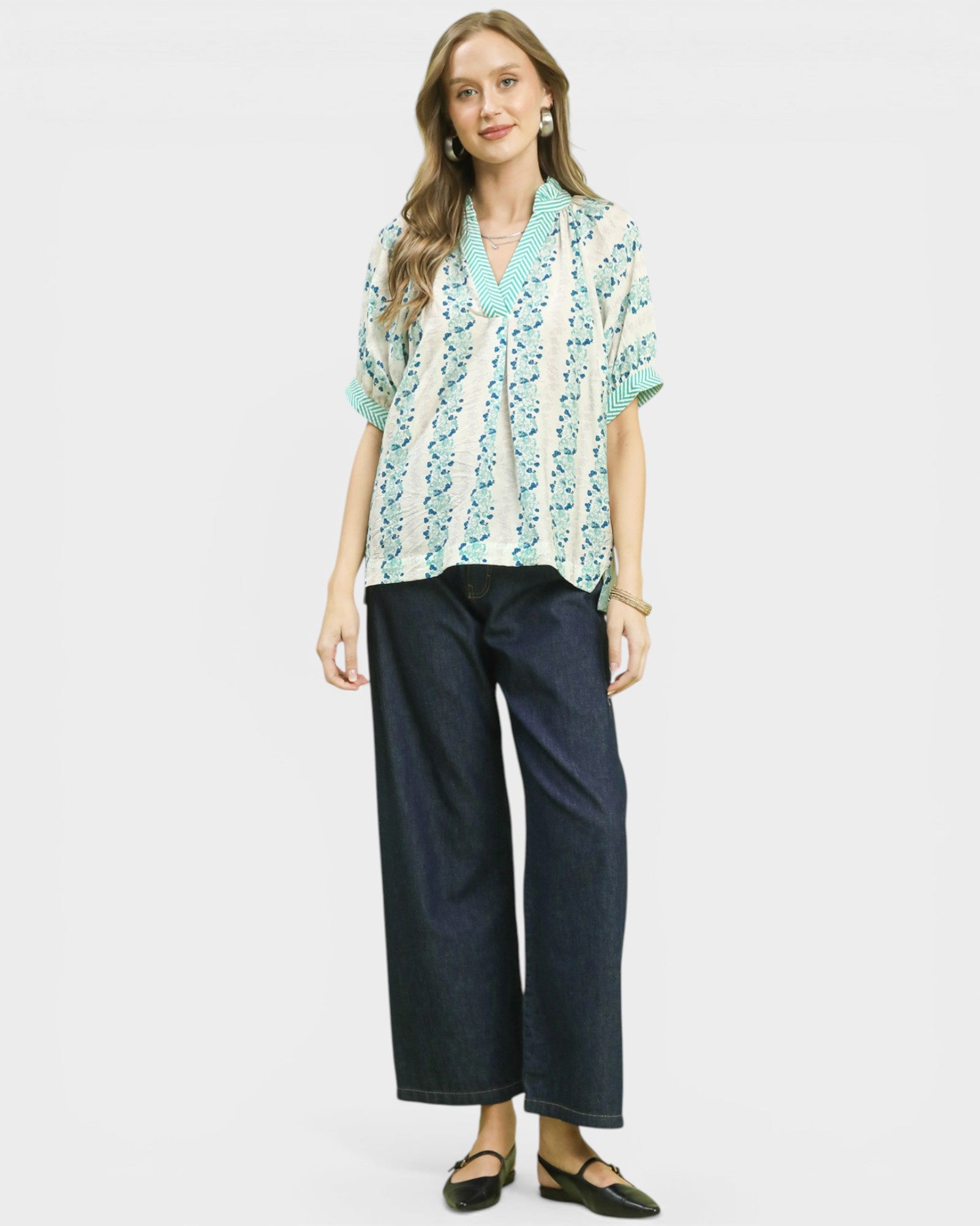 Woman wearing a patterned blouse and dark pants on a white background