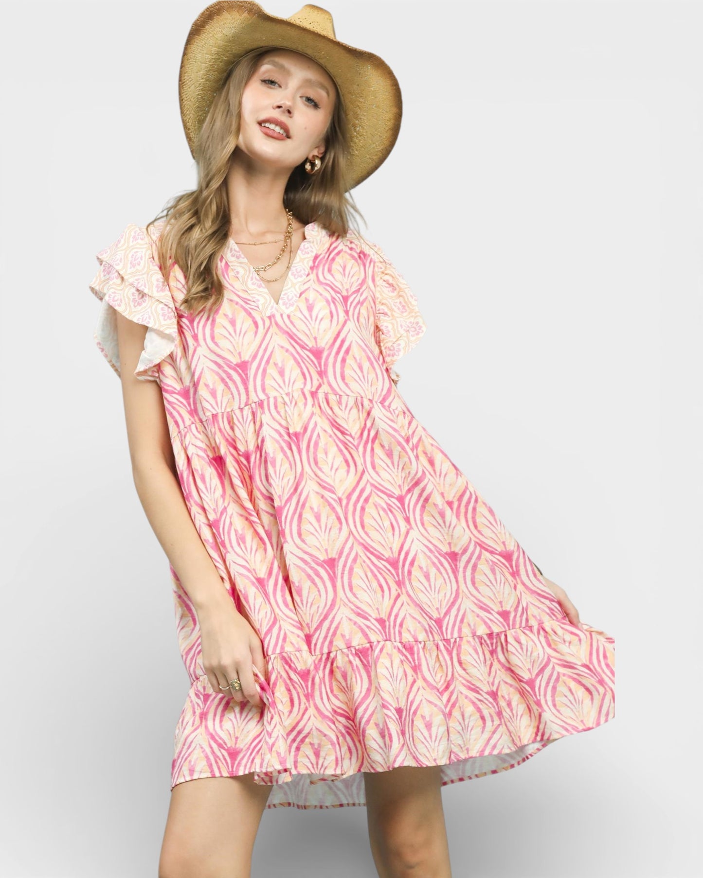 Woman wearing a pink and white patterned dress with a straw hat on a plain background
