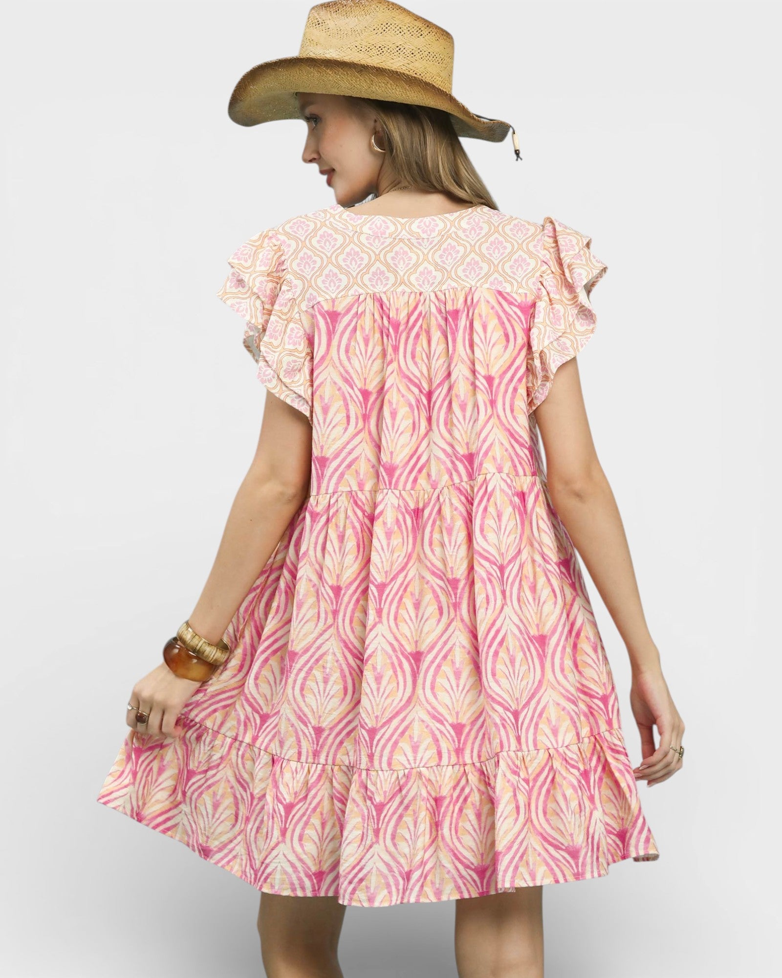 Woman wearing a pink and white patterned dress with a straw hat on a plain background