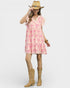Woman wearing a pink patterned dress, tan cowboy boots, and a straw hat on a white background